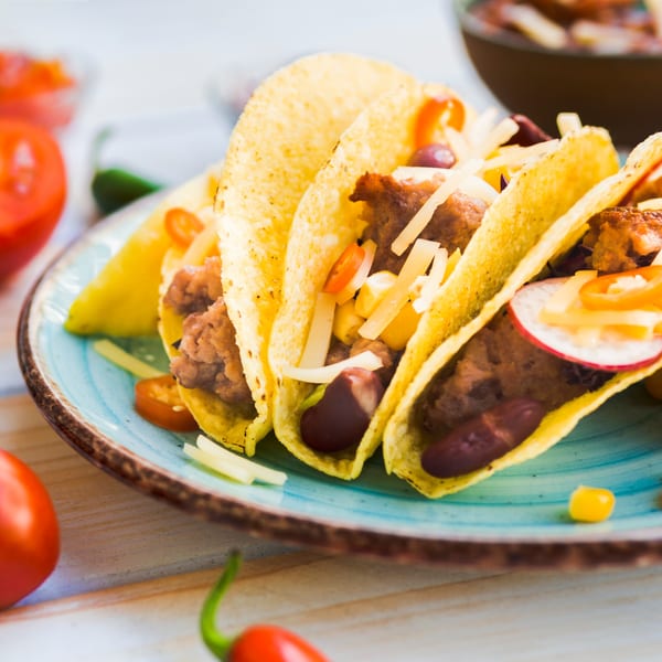 Three Mixteca Grill tacos filled with meat, beans, cheese, and vegetables on a blue plate.