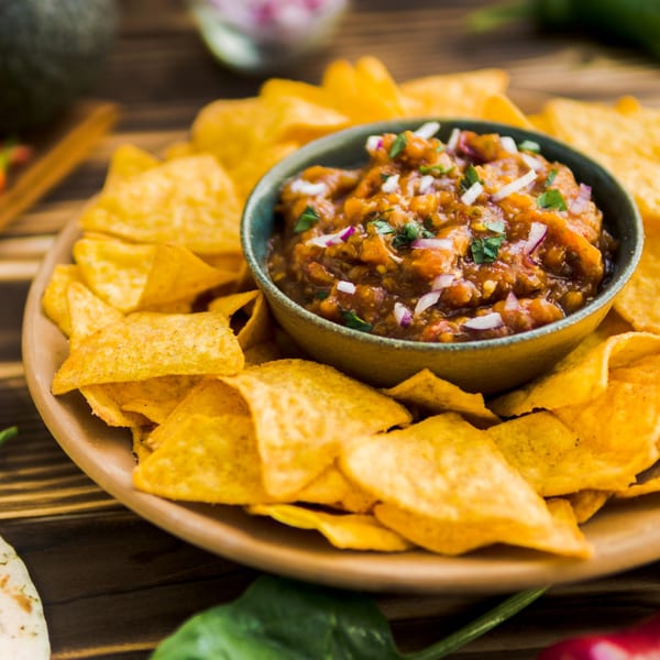 A bowl of Mixteca Grill's salsa with red onions and cilantro, surrounded by tortilla chips.