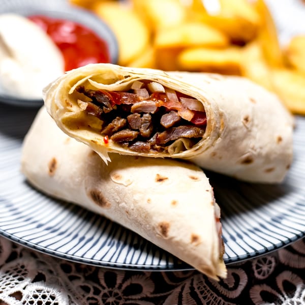 Two Mexican burritos, cut in half, revealing meat, onions, and sauce, with fries and dips in the background.
