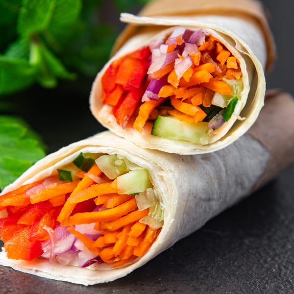 Two colorful Mexican wraps filled with shredded carrots, red peppers, red onions, and cucumbers.