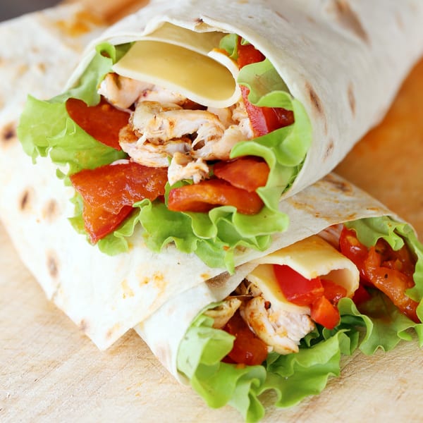 Two chicken wraps with lettuce, cheese, and red peppers on a wooden surface.